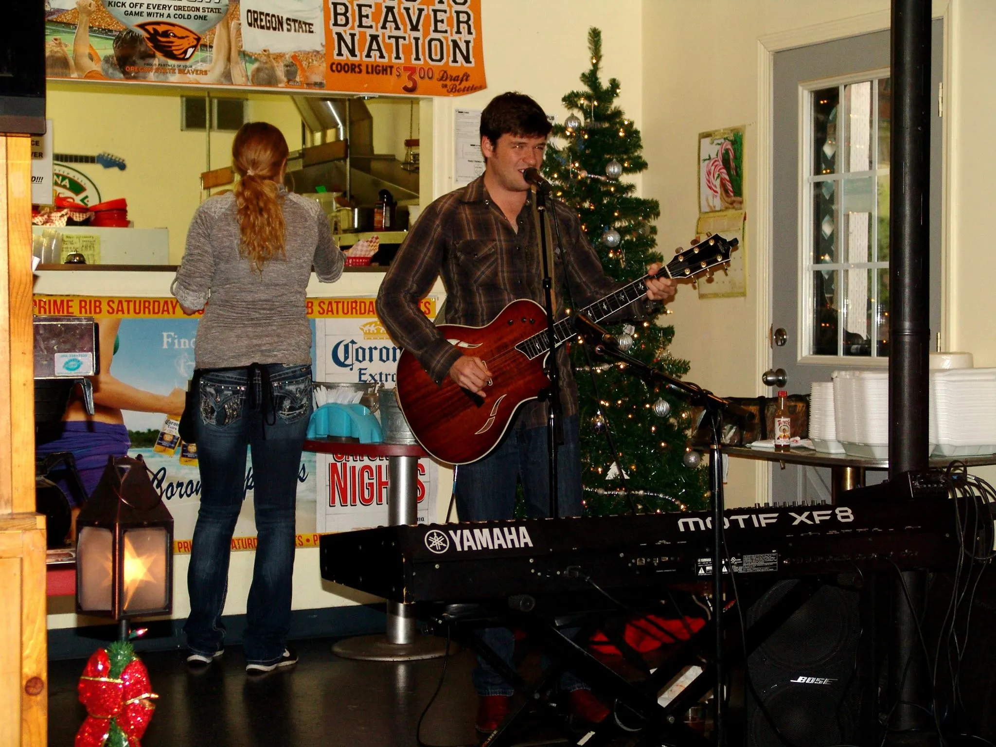 Singer playing guitar on stage with the Christmas tree lit behind her.