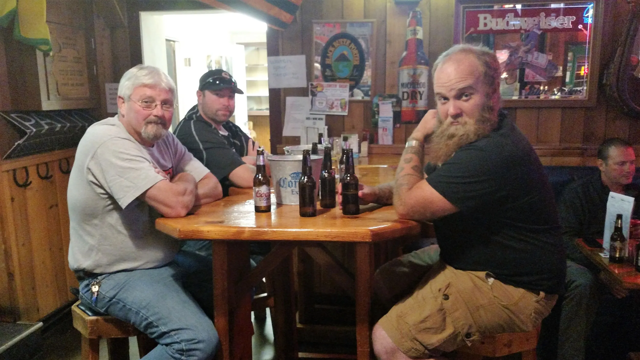 Three friends at a wooden table with beer bottles, the wood interior warm behind them.